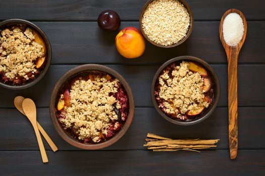 Overhead shot of rustic bowls filled with baked plum and nectarine crumble or crisp, photographed on dark wood with natural light