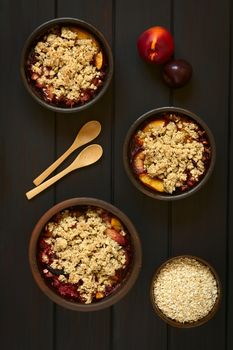 Overhead shot of rustic bowls filled with baked plum and nectarine crumble or crisp, photographed on dark wood with natural light