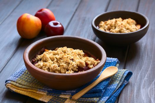 Two rustic bowls filled with baked plum and nectarine crumble or crisp, photographed on dark wood with natural light (Selective Focus, Focus one third into the first dessert)