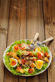 Salad Caesar with mushrooms, eggs, chili and radish with two forks on wooden background with space vertical