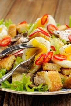 Salad Caesar with mushrooms, eggs, chili and radish with two forks on wooden background closeup vertical