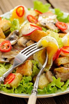 Salad Caesar with mushrooms, eggs, chili and radish with two forks on wooden background closeup vertical