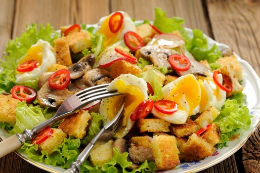 Salad Caesar with mushrooms, eggs, chili and radish with two forks on wooden background closeup horizontal