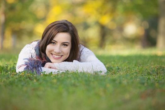 Happy smiling young woman laying down on grass