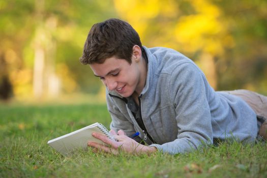 Smiling Caucasian teenager laying down on grass doing homework