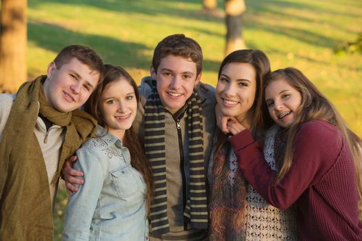 Group of five cheerful youth outdoors embracing
