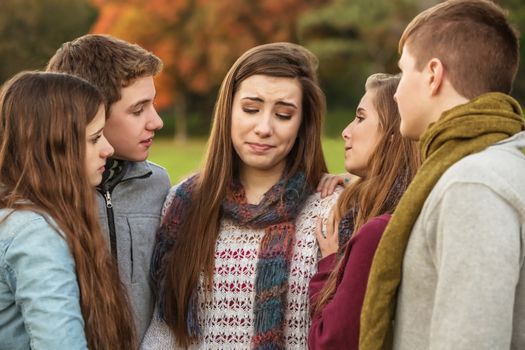Crying teen in scarf with sympathetic friends outdoors