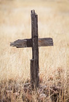 Decayed wooden crucifix tied with wire in overgrown weeds