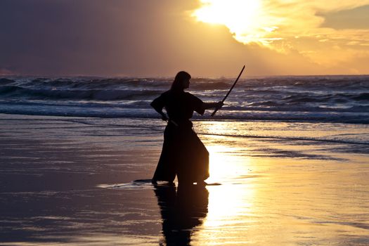 Young samurai women with Japanese sword(Katana) at sunset on the beach