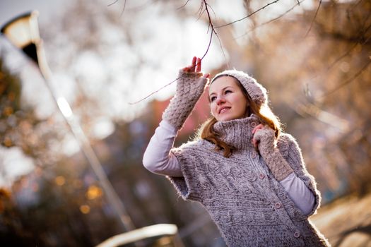 Autumn/winter portrait: young woman dressed in a warm woolen cardigan posing outside in a city park