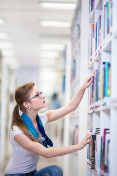 Pretty, female college student in a library, looking for a book (shallow DOF; color toned image)