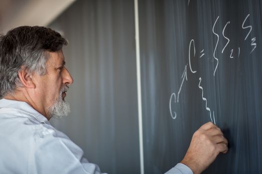 Senior chemistry professor writing on the board while having a chalk and blackboard lecture (shallow DOF; color toned image)