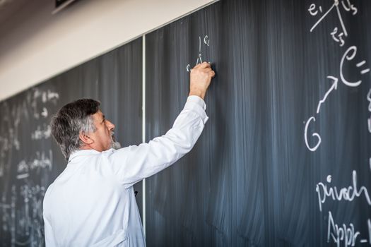 Senior chemistry professor writing on the board while having a chalk and blackboard lecture (shallow DOF; color toned image)