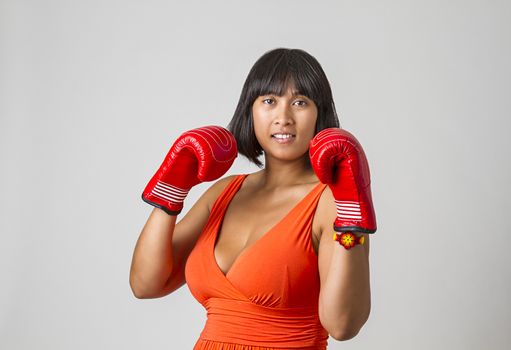 Young sexy philipino woman, wearing a low cut orange dress, with her gloved fists up