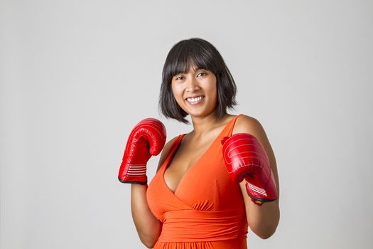 twenty something asian woman wearing a low cut orange dress with great smile gearing up for a punch