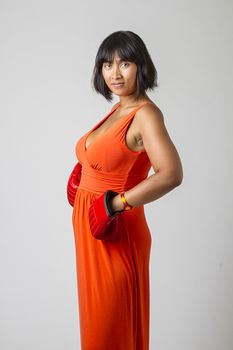 twenty something asian woman wearing a low cut orange dress and boxing glove