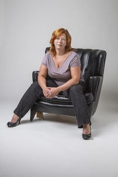 woman in her forties with red hair sitting on a black leather love set