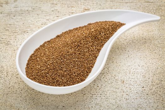 gluten free teff grain on a teardrop shaped bowl against white painted grunge wood