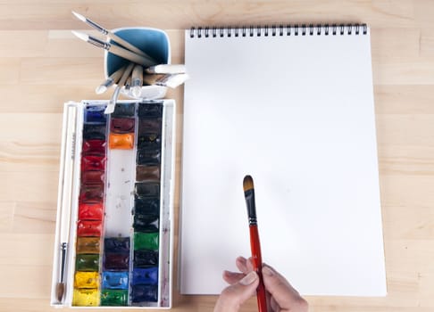 Beautiful composition of watercolor paints, brushes, album artist, with the artist's hand.