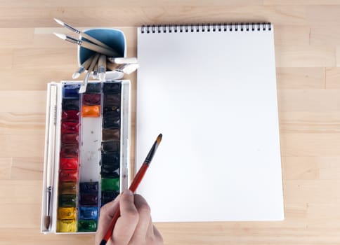 Beautiful composition of watercolor paints, brushes, album artist, with the artist's hand.