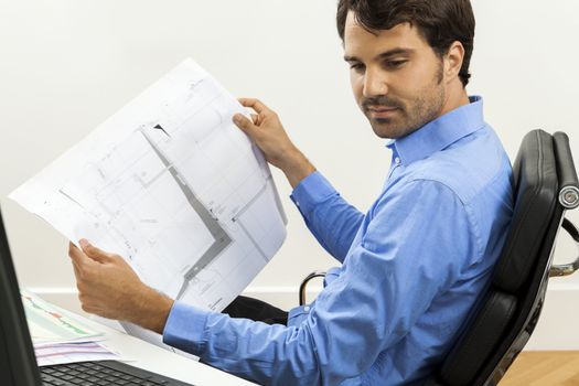 Young handsome man sitting at his desk in the office while reading written agreements and studying important documentation for work