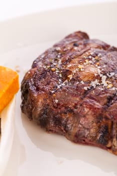 Delicious trimmed lean portion of thick grilled beef steak with seasoning served on a white plate, close up with shallow dof