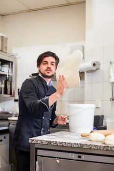 Professional cook or chef in a commercial kitchen tossing dough while making pastries for desserts in a restaurant or hotel