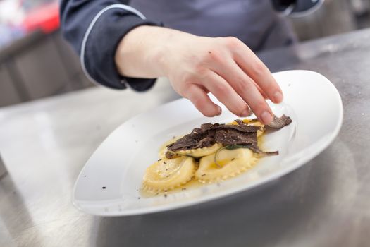 Chef grating truffle mushroom shavings onto homemade ravioli in a restaurant kitchen while preparing a dinner, close up view of the counter, plate and hands
