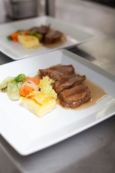 Chef plating up food in a restaurant pouring a gravy or sauce over the meat before serving it to the customer, close up view of his hand and the gravy boat