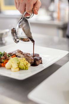 Chef plating up food in a restaurant pouring a gravy or sauce over the meat before serving it to the customer, close up view of his hand and the gravy boat