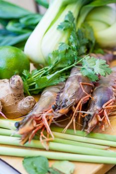 Ingredients for Thai tom yam soup laid out on a kitchen counter with tiger prawns, mushrooms, ginger, lemongrass, limes, celery, parsley and spices