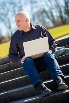 High angle profile view of a balding middle-aged man sitting on a wooden bench using a laptop computer