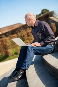 High angle profile view of a balding middle-aged man sitting on a wooden bench using a laptop computer