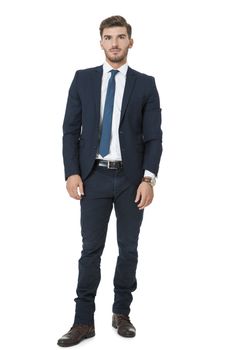 Stylish successful handsome young businessman standing in a relaxed pose with his hands in his pockets and his suit jacket open, isolated on white