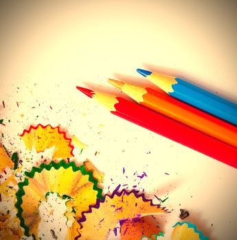 three colored pencils and shavings on white background with copy space. instagram image retro style