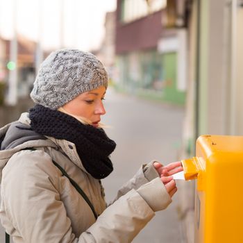 Young woman posting a letter, dropping an envelope in a postbox.