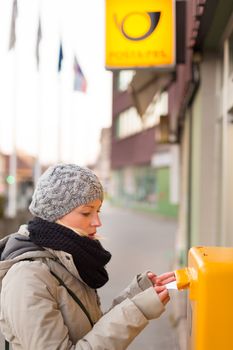 Young woman posting a letter, dropping an envelope in a postbox.