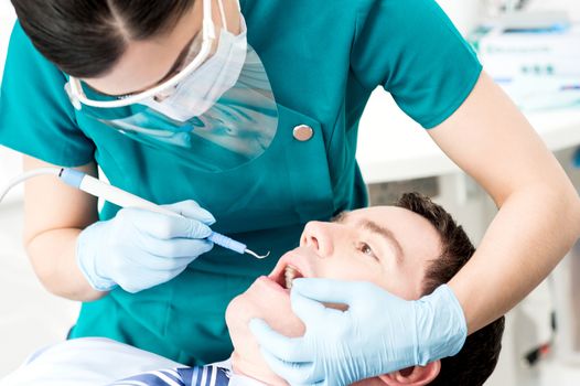 Female dental assistant treat male patient in clinic 