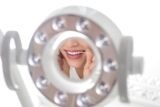 Woman flossing her teeth infront of light mirror