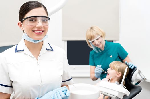 Smiling dentist, assistant examining a patient behind