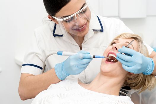 Smiling female dentist procedure of teeth cleaning