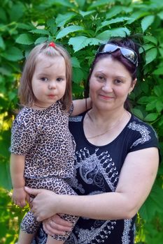 Grandmother with her granddaughter in her arms on the background of green