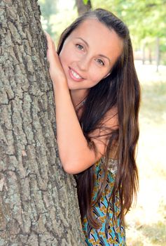 Portrait of a young girl hid behind a tree trunk