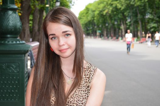 Portrait of a young girl sitting in a park on a background of green trees and alleys