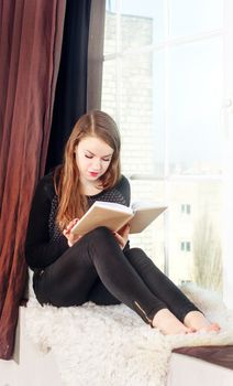 Young girl reading book near the window.
