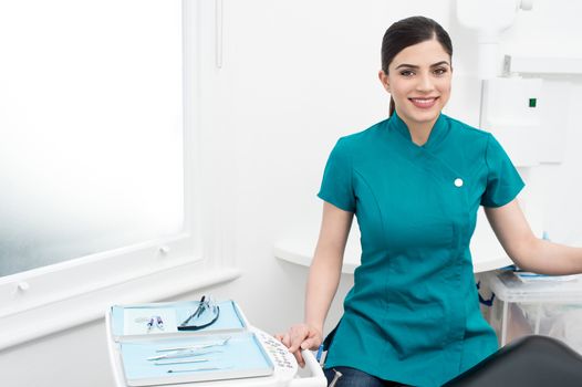 Smiling female assistant sitting beside tools tray