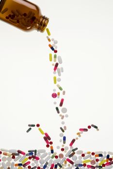 Drugs Pouring from a Medicine Bottle and splashing into a sea of tablets, pills and capsules.