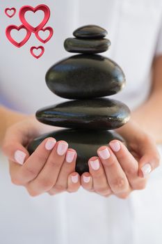 Beauty therapist holding pile of stones for massage against pink hearts