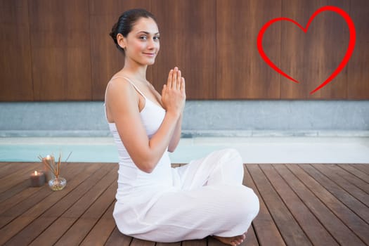 Content brunette in white sitting in lotus pose smiling at camera against heart