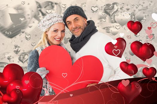 Smiling couple in winter fashion posing with heart shape against grey valentines heart pattern